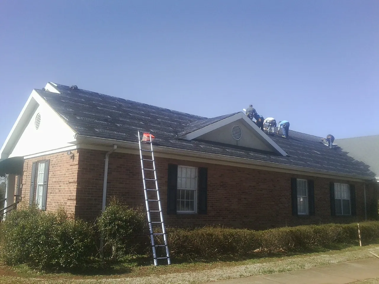 Crew tearing shingles off a brick ranch roof with a ladder set — Emergency Roof Repair work by our crew in Pollock Pines