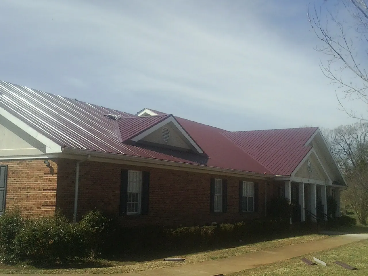 Red metal roof with gabled entries on a long brick building, from a Hail Damage Roof Repair job in Pollock Pines