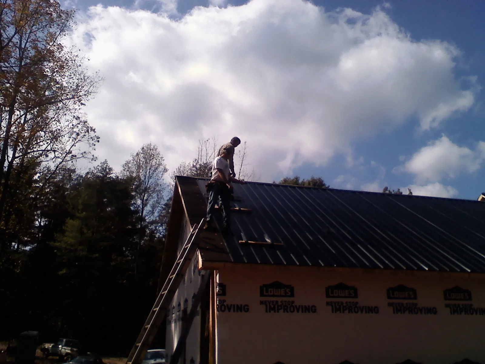 Roofer fastening dark metal panels high against a cloudy sky, from a Roof Inspection job in Pollock Pines